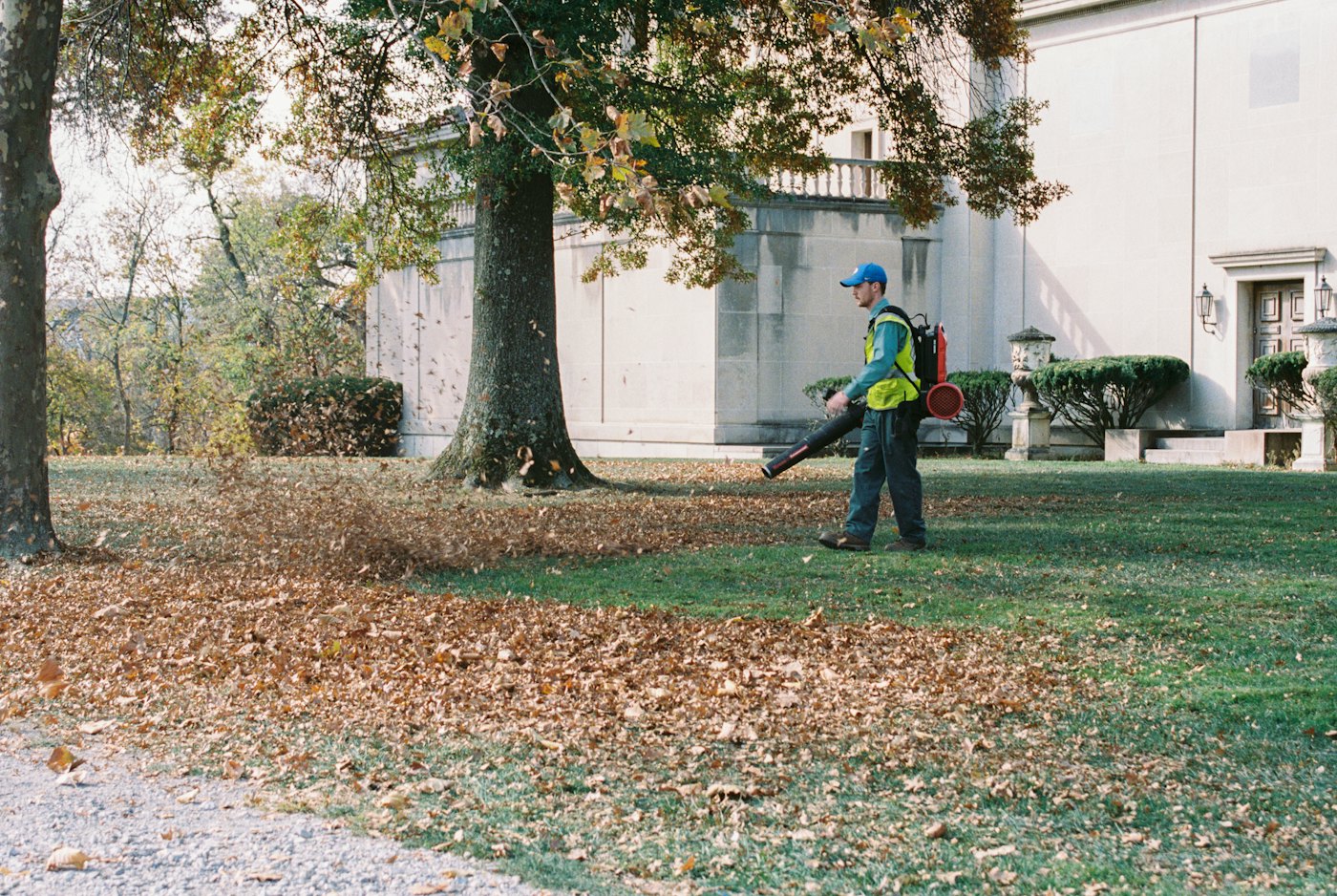 Mitarbeiter entfernt Herbstlaub mit einem Laubbläser von einer Rasenfläche